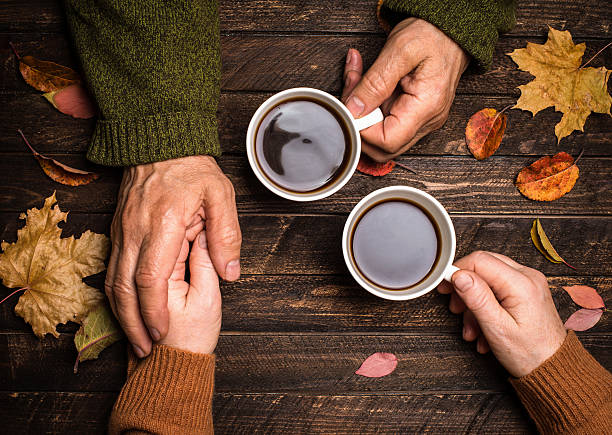 Mãos de uma pessoa idosa segurando uma xícara de café, luz suave da tarde entrando pela janela